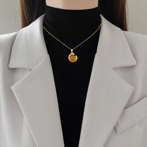 Elegant gold titanium steel necklace with amber sphere pendant worn on white blazer