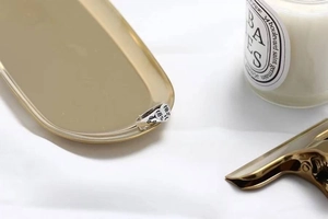 Silver sadness face ring displayed on a golden tray with a luxury candle background