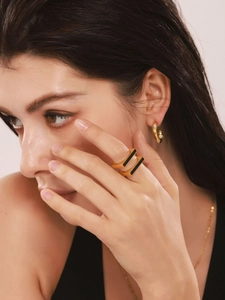 Detail of a minimalist 18K gold plated ring with black enamel and diamond hoop earrings