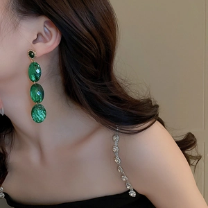 Gros plan de boucles d'oreilles pendantes en acrylique vert portées avec détails dorés