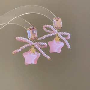 Close-up of pink bow and star earrings with faux crystals on a display stand