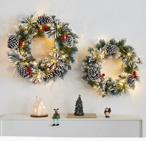 Close-up of Christmas wreath with snow-flocked pine needles, red berries and LED lights
