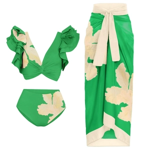 Detailed flat lay of a green three-piece floral bikini set with ruffles and beach sarong