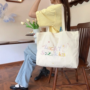 Photo lifestyle artistique d'un sac cabas en toile crème avec broderie colorée chance