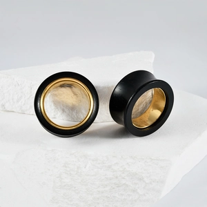 Dual-tone black sandalwood and gold stainless steel hollow ear gauges on white stone