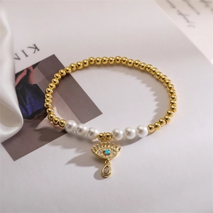 Detailed view of gold beads and pearls bracelet with crystal evil eye and teardrop charm