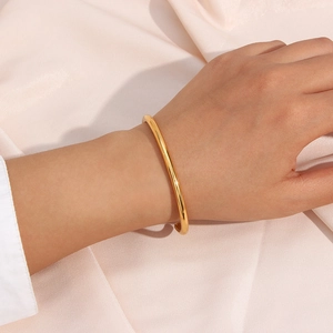 Close-up of a minimalist 18K gold plated stainless steel open bangle on pink silk