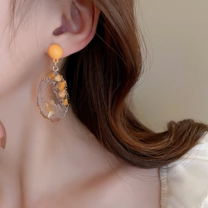 Close-up of geometric irregular resin earrings with orange beads on model