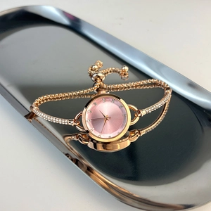 Detail of rose gold quartz watch with pink rhinestone dial and bracelet strap on metal tray