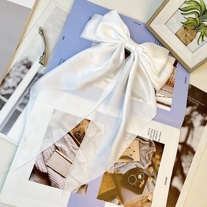 Close-up of a large white satin bow hair clip with long ribbons on a magazine background