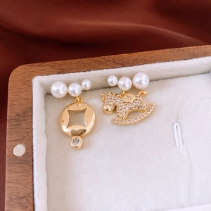 Detailed close-up of 18K gold plated asymmetric horse and coin pearl earrings on velvet