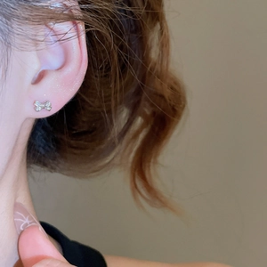 Close-up of bow-shaped stud earrings with zircons worn by a model in warm light