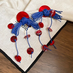 Detail of red shell disc earrings with blue braided rope on rustic fabric background