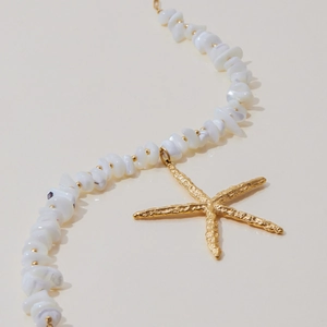 Macro detail of 18K gold stainless steel starfish pendant and natural white beads