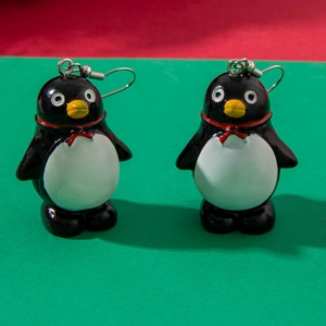 Close-up of cute cartoon penguin earrings with red Santa hats and metal hooks