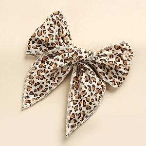 Top view of a soft leopard print fabric bow hair clip on a minimalist beige surface