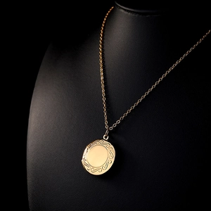 Detailed close-up of a vintage golden round locket necklace on a black jewelry bust display