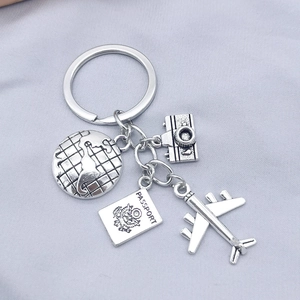 Silver travel keychain with globe, camera, passport, and airplane charms on gray fabric