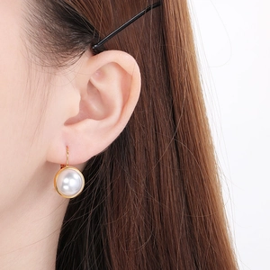 Detail of round shell pearl earrings with gold titanium steel trim worn by model
