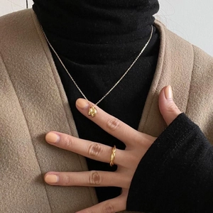 Detail of 18K gold-plated key necklace and rope ring on a model wearing a black turtleneck