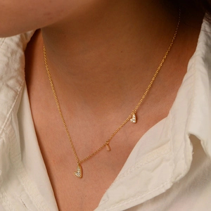 Detailed close-up of a gold necklace featuring three heart pendants with sparkling zircon