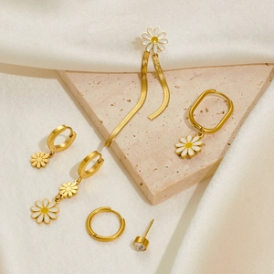 Detail of gold daisy earrings set with enamel flowers and tassel on stone base