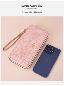 Pink double zipper long wallet with floral embossing and wrist strap next to a phone