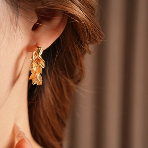 Close-up of gold-plated leaf drop earrings worn by a model in a natural setting