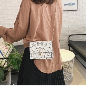 Close-up of a white geometric paneled chain shoulder bag worn by a model in casual style