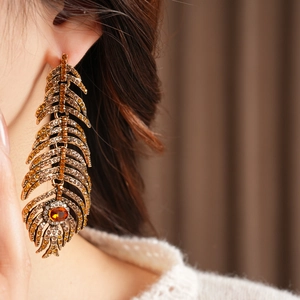 Close-up of vintage feather earrings with amber crystals and orange stones on a model
