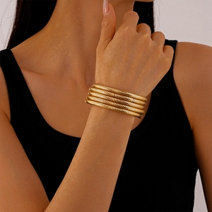 Detail of layered gold snake chain cuff bracelet with textured metallic finish on wrist