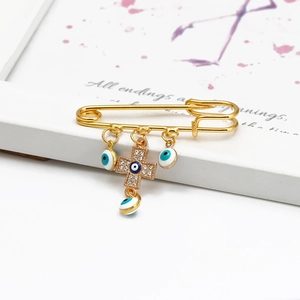 Detail of gold safety pin brooch with sparkling rhinestone cross and blue evil eye charms