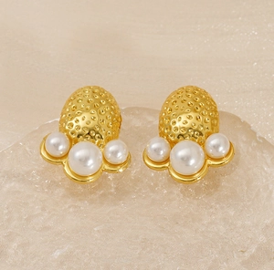 Macro shot of gold hammered metal earrings with three white pearls on silk background