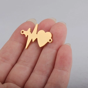 Detailed macro view of a small golden heartbeat charm connector held on a fingertip