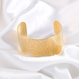 Detailed close-up of wide hammered gold cuff bracelet on white satin fabric background