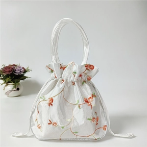 Detail of white satin drawstring pouch with orange floral embroidery and silk handles