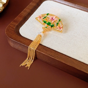 Close-up of fan-shaped 18K gold brooch with enamel flowers, pearl, and tassel details
