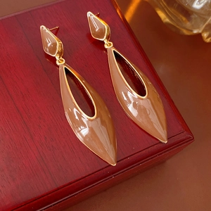 Detailed close-up of vintage golden enamel teardrop earrings on a wooden jewelry box