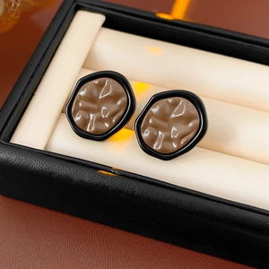 Detail of geometric brown resin earrings with black trim and vintage pleated texture