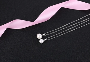 Detail showing two sizes of white pearl pendants on elegant silver chain necklaces