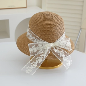 Close-up of children straw hat with delicate white lace ribbon and bow on gold stand