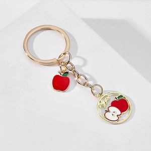 Detailed view of golden alloy keychain with red enamel apple charms on white surface