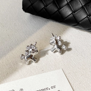 Macro shot of silver unicorn stud earrings with zircon inlay on beige fabric background