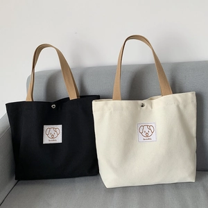 Detail view of canvas tote bags in black and beige with cute dog patches and metal snaps
