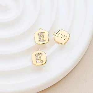 Macro detail of gold-plated square pendant with letter E inlaid with sparkling zircons