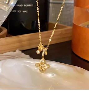 Detailed close-up of a gold clover pendant with crystals on a white seashell tray