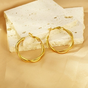 Detail of gold twisted hoop earrings on stone display with silk background texture