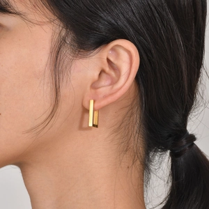 Close-up of a model wearing a minimalist gold-plated rectangular geometric huggie earring