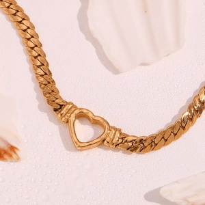 Close-up of 18K gold-plated hollow heart pendant on flat curb chain over shell background