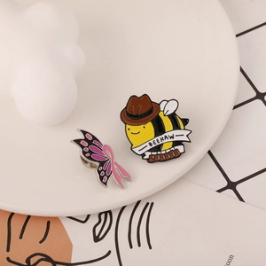 Detail of enamel butterfly and cowboy bee pins with Beehaw text on white ceramic plate